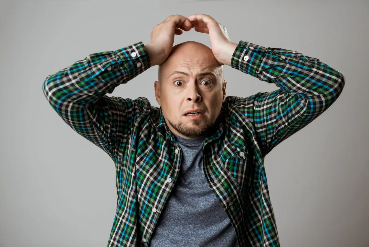 Upset emotive young man grab his head over beige background. Copy space.