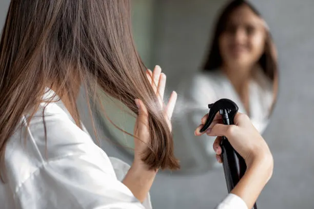 Haircare. Young Female Applying Hair Spray While Standing Near Mirror In Bathroom, Unrecognizable Millennial Woman Testing New Hairstyle Product At Home, Selective Focus On Her Reflection